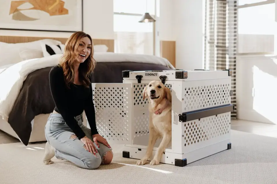 A person&#x27;s hand resting near a puppy inside an open crate door