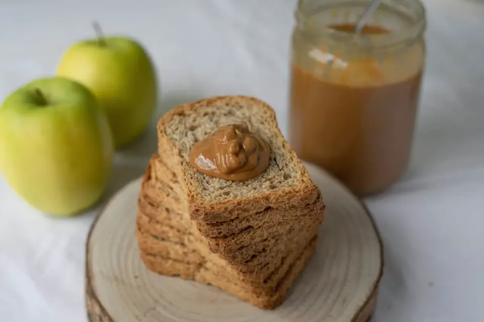 Open jar of peanut butter with a spoon, positioned near a dog treat